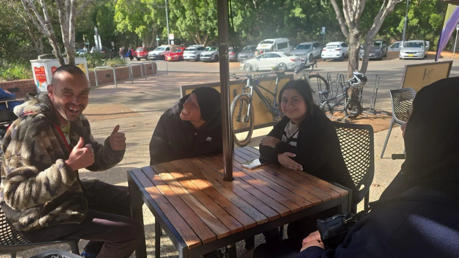 Four Focus participants and a support worker sitting around an outdoor café table in the winter sun, laughing.