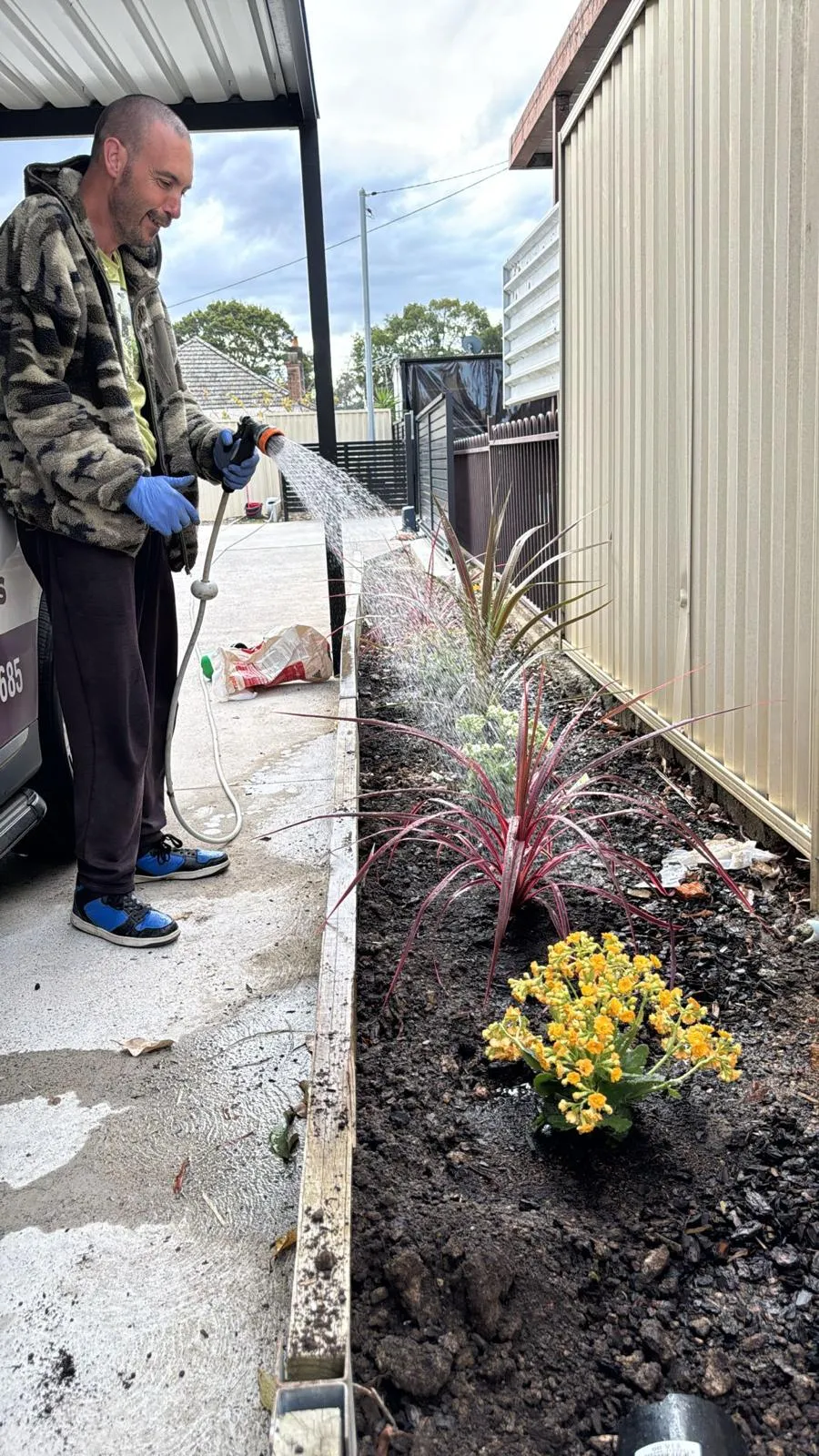 A Focus participant watering a newly planted garden bed with a hose.