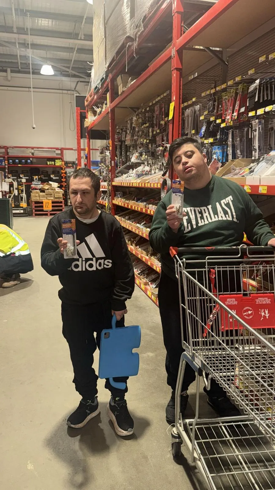 Two Focus participants holding up hardware they picked out, pushing a trolley through the aisle.