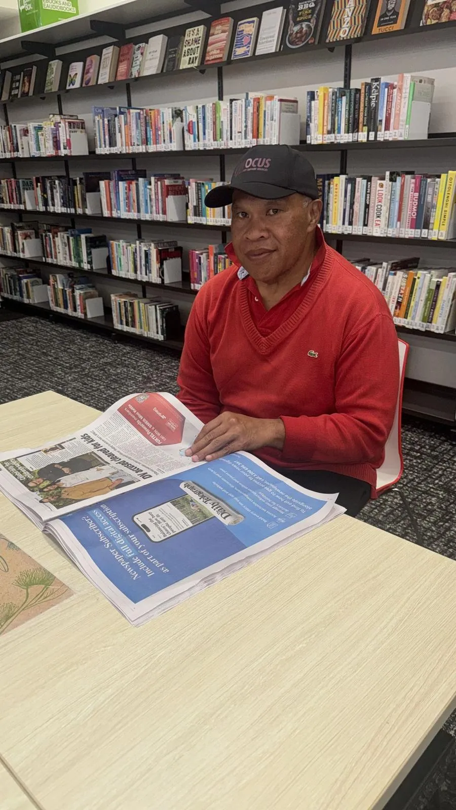 A Focus participant in a Focus cap reading the newspaper at the local library.
