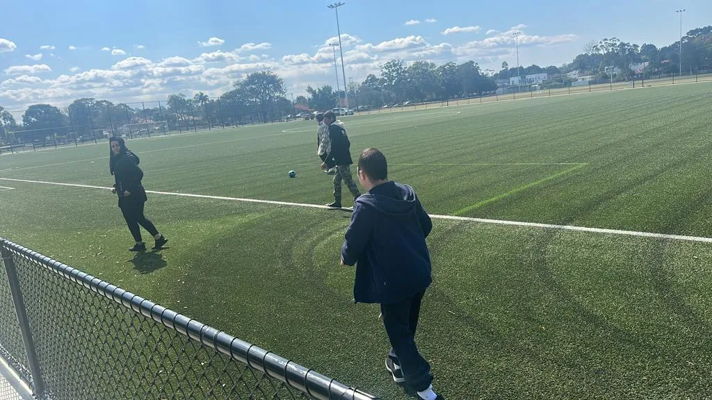 Three people from Focus passing a soccer ball around a green playing field under a bright winter sky.