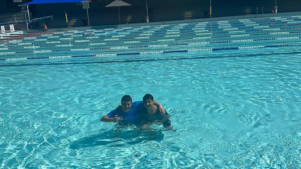 A support worker and a Focus participant with their arms around each other in a public swimming pool.